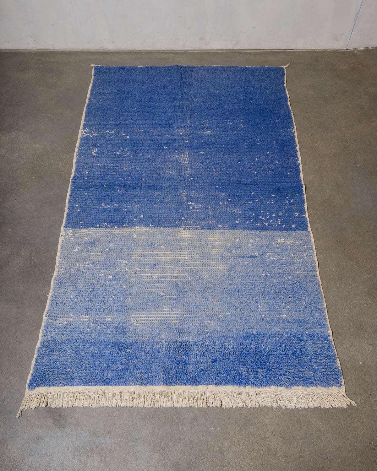 Blue rug with white fringe on a gray floor